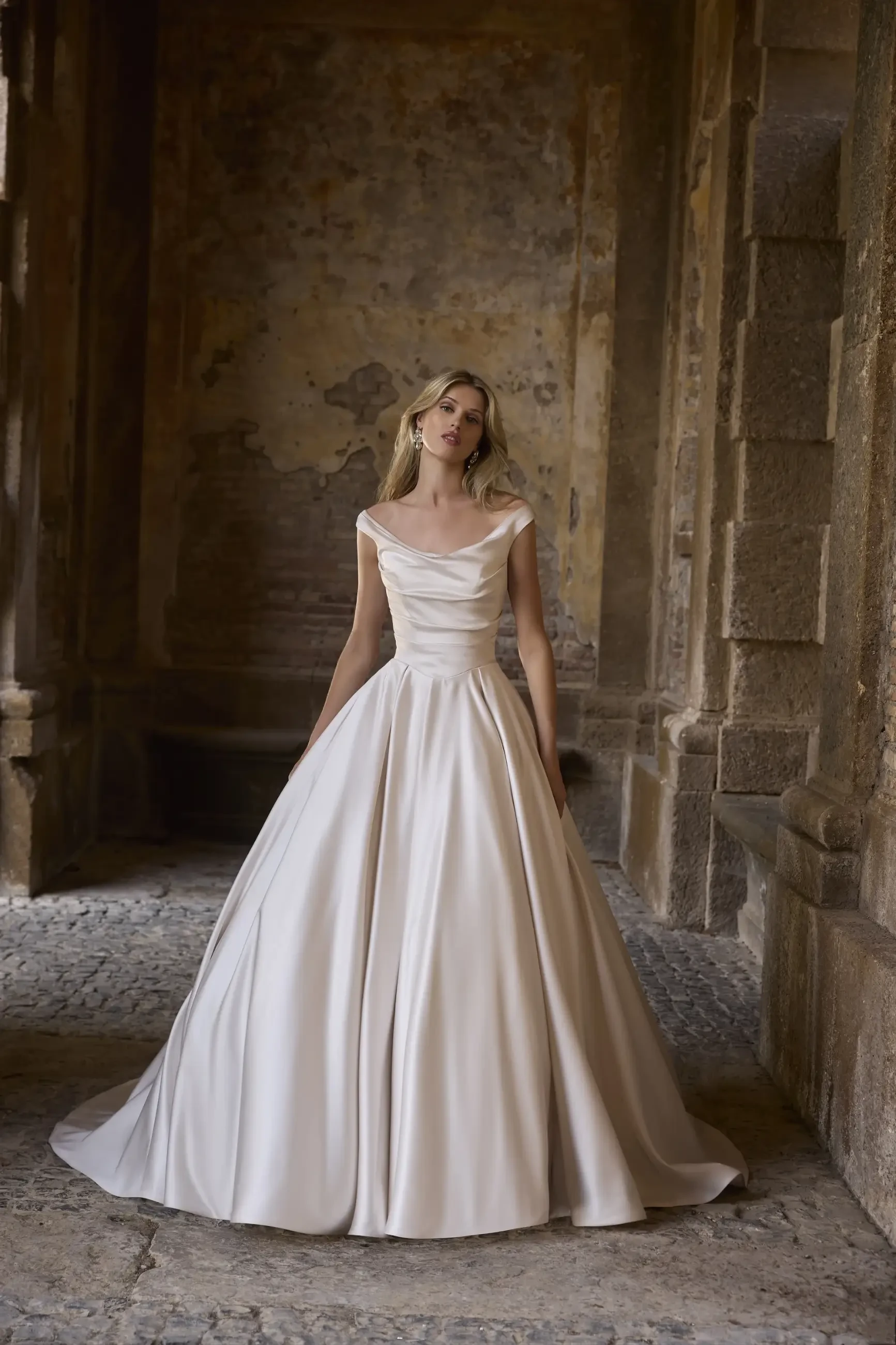 A woman in a flowing white gown stands in an ornate, historic corridor.