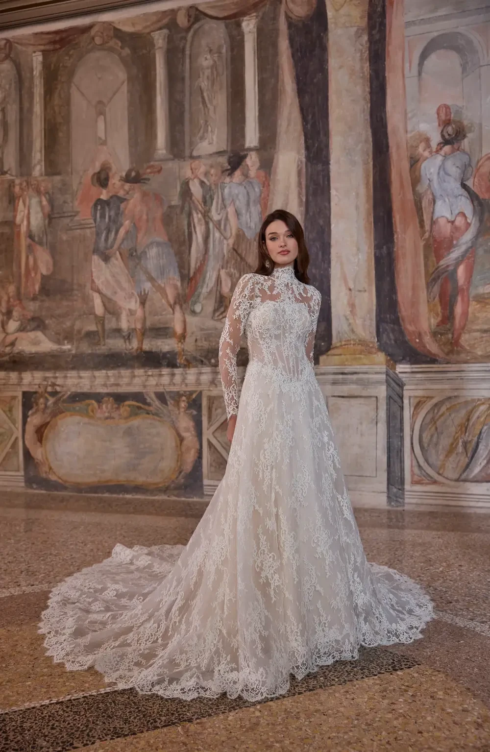 A woman in a stunning lace wedding dress, standing gracefully in front of a historical mural.